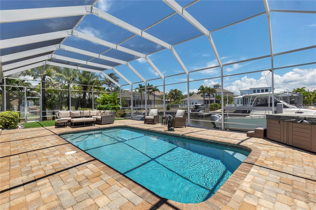 A screened-in pool patio features stone pavers, outdoor furniture, and a view of a canal — 5727 SEA TROUT PLACE, APOLLO BEACH, FL