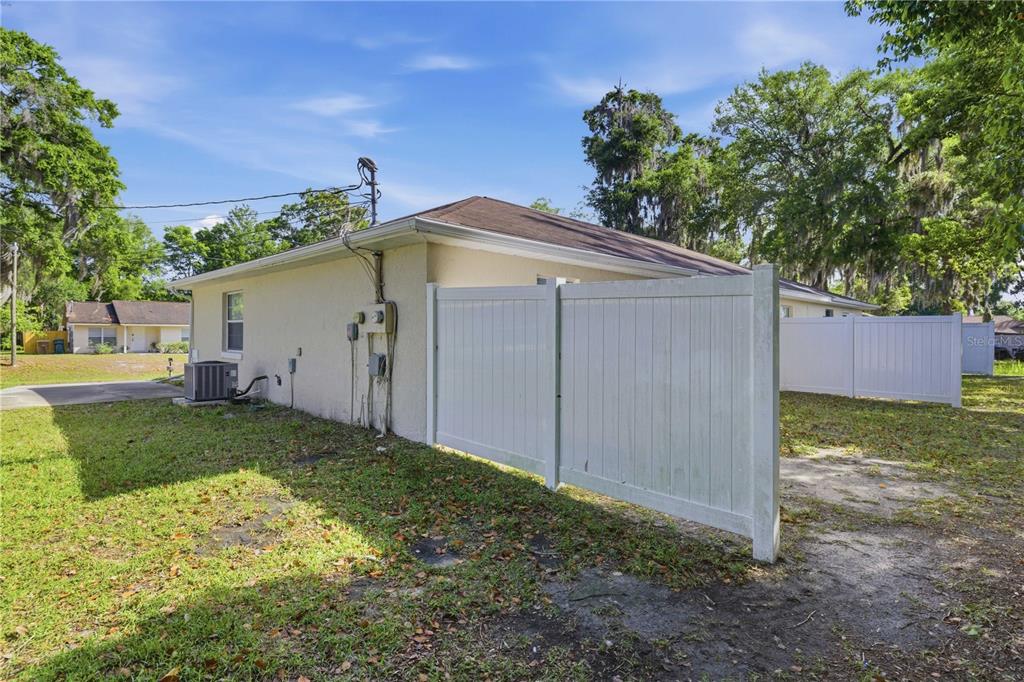 The side exterior of a stucco house features a white vinyl fence and an AC unit — 712 NE 26TH STREET, OCALA, FL