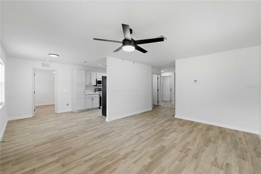 A bright living area features light wood-look tile flooring, a ceiling fan, and white walls — 712 NE 26TH STREET, OCALA, FL