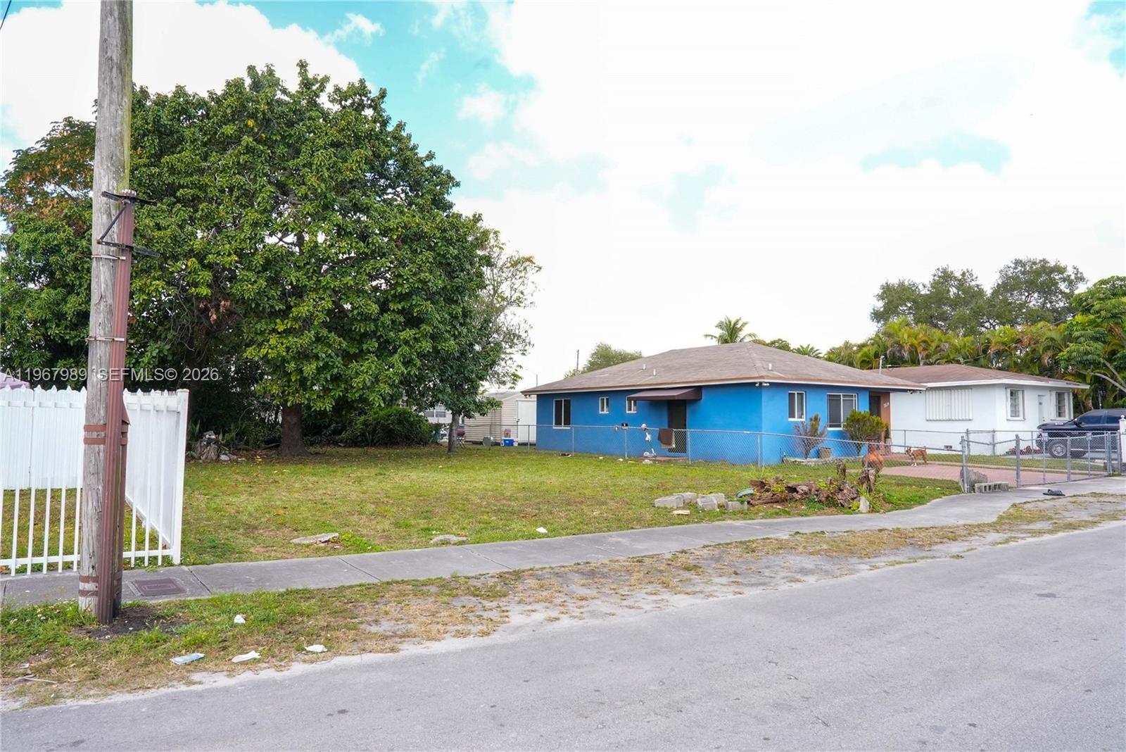 A blue single-story house sits on a grassy lot next to a large tree — 7610 NW 15th Ave, Miami FL 33147, MIAMI, FL