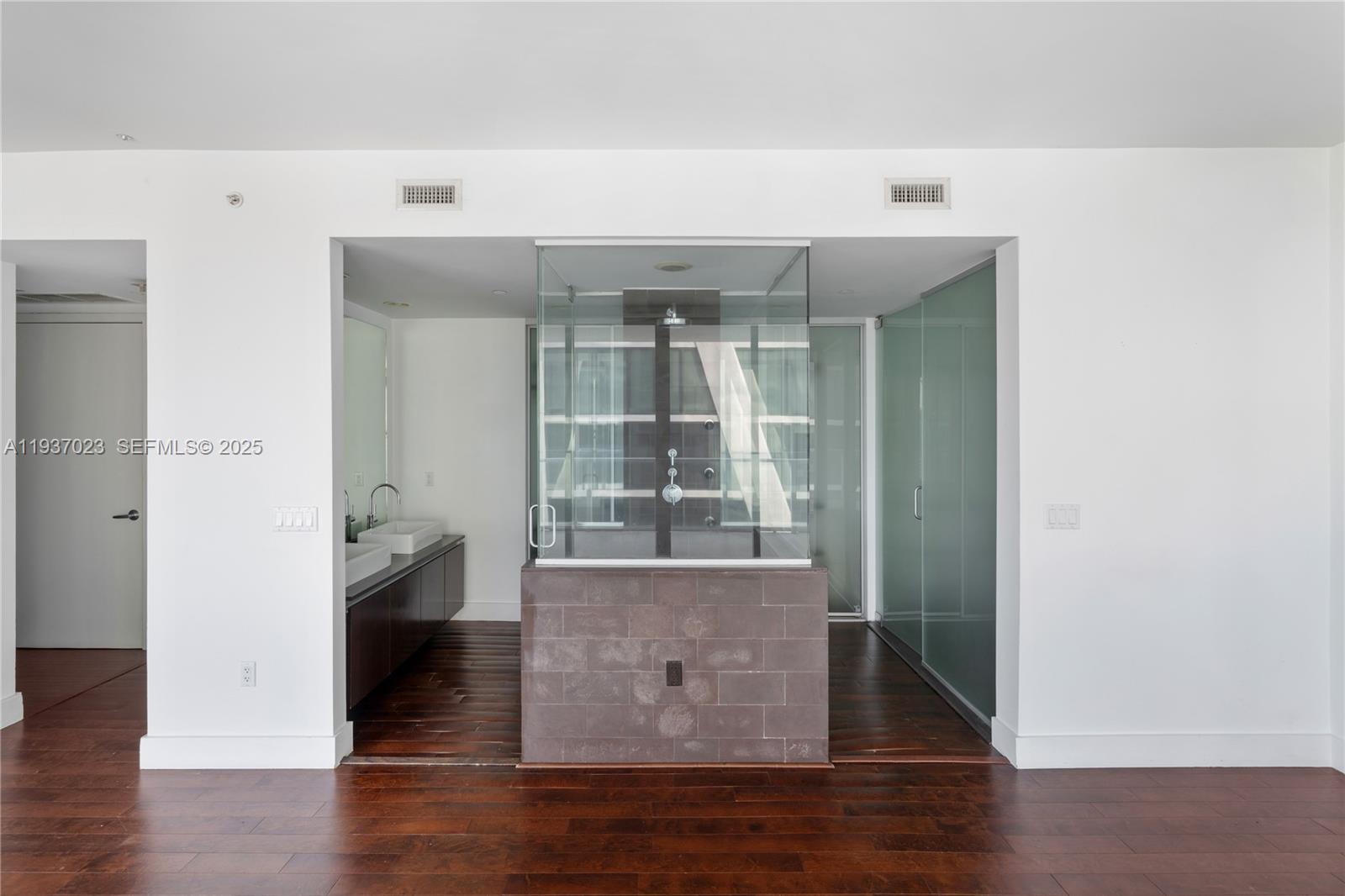 A modern bathroom features a central glass-enclosed shower, dark wood flooring, and a double vanity — 1040 Biscayne Blvd # 4108, Miami FL 33132, MIAMI, FL