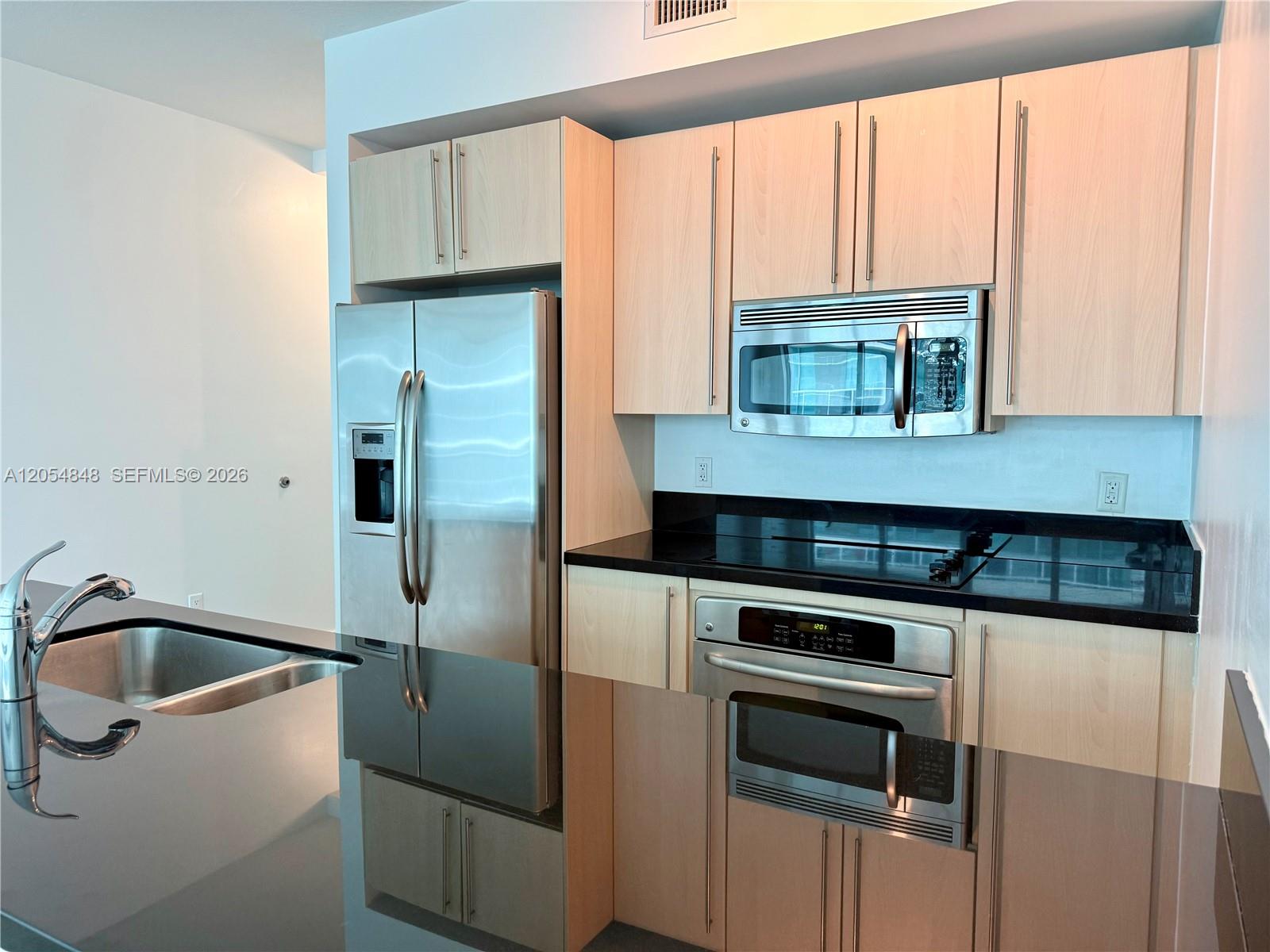 A kitchen features light wood cabinets, stainless steel appliances, and black countertops — MIAMI, FL