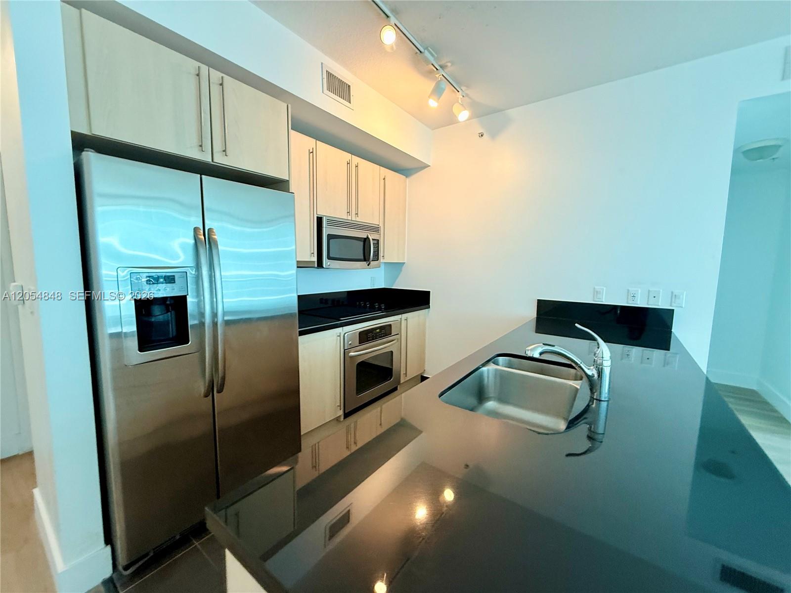 A modern kitchen features light wood cabinets, stainless steel appliances, and a black countertop island — MIAMI, FL