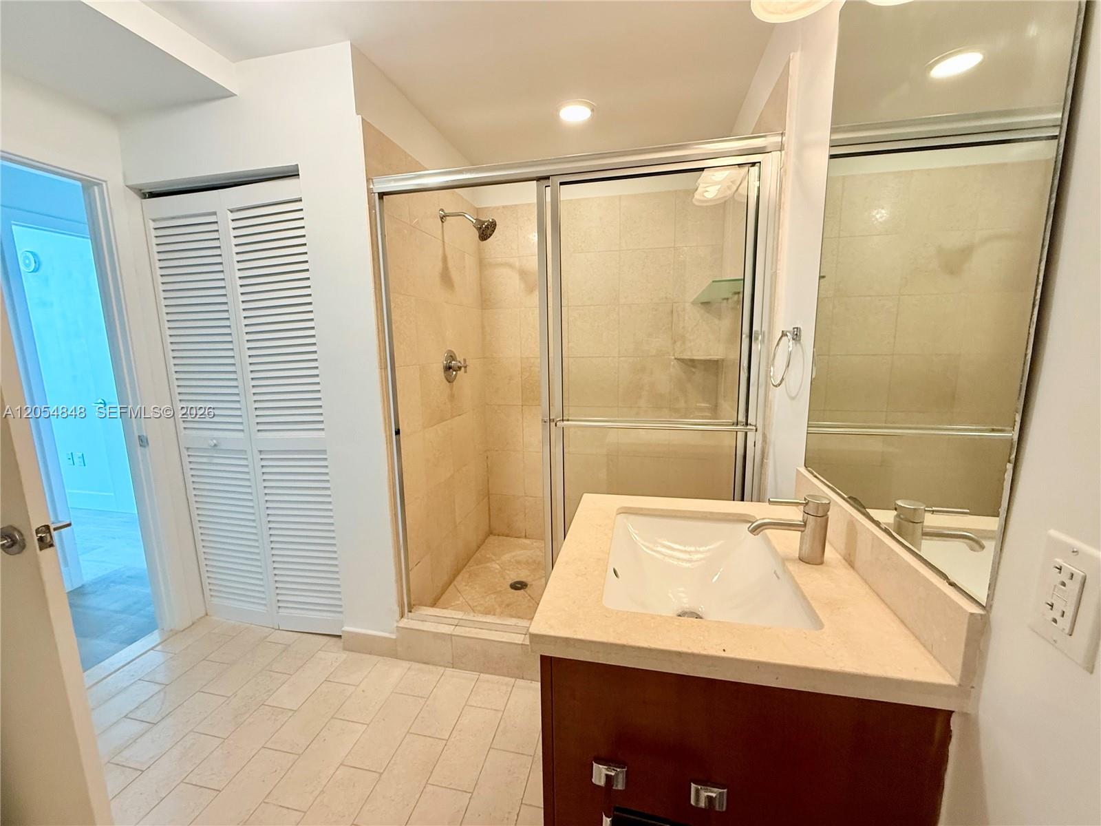 A bathroom features a glass-enclosed shower, a vanity with a stone countertop, and tiled floors — MIAMI, FL