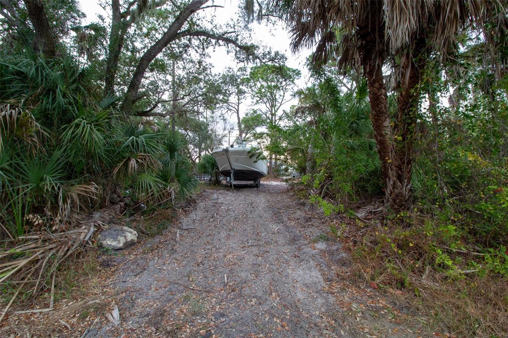 A boat on a trailer sits at the end of a dirt path surrounded by trees — 15038 CRESENT AVENUE, PORT CHARLOTTE, FL