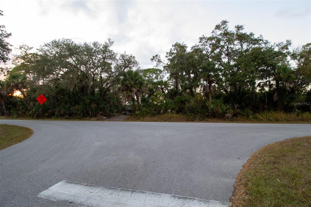 A paved road intersection sits in front of a dense, wooded area with mature trees — 15038 CRESENT AVENUE, PORT CHARLOTTE, FL