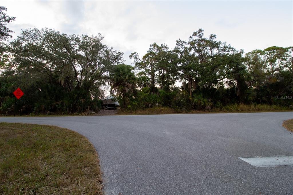 A paved road intersection leads to a wooded lot with a boat parked in the distance — 15038 CRESENT AVENUE, PORT CHARLOTTE, FL