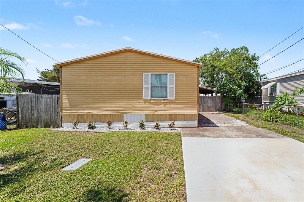 A single-story yellow mobile home features a central window and a concrete driveway — 739 DRIFTWOOD LANE, TARPON SPRINGS, FL