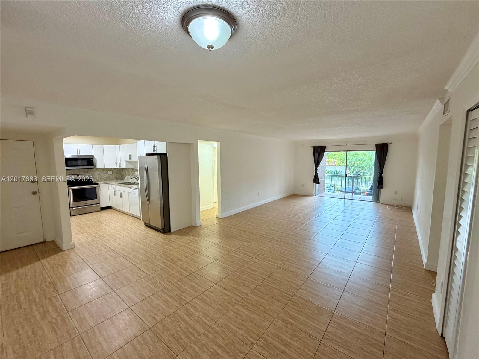 An open-concept living area features tiled floors, a white kitchen, and a sliding glass door — 9429 SW 76th St # W25, Miami FL 33173, MIAMI, FL