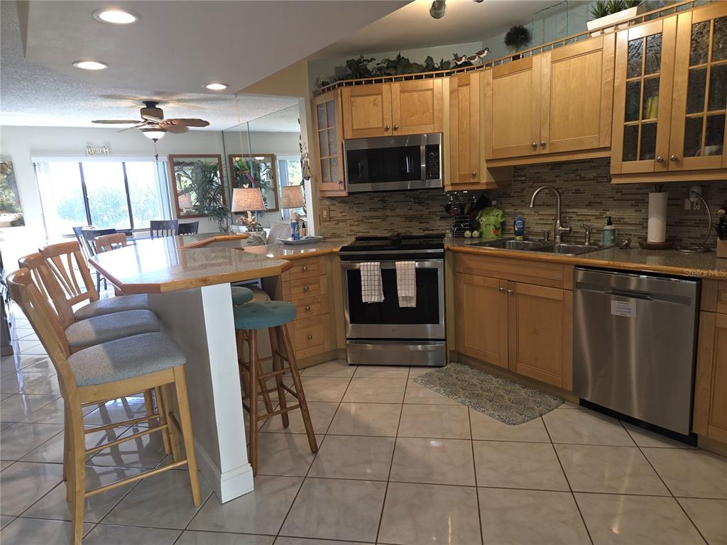 A kitchen features light wood cabinets, stainless steel appliances, a breakfast bar, and tiled floors — 1515 PINELLAS BAYWAY S UNIT A6, TIERRA VERDE, FL