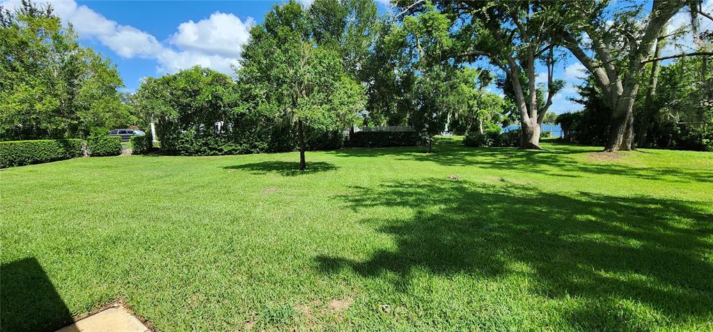 A large, grassy backyard features mature trees and a glimpse of a lake beyond — 7864 BROKEN ARROW TRAIL, WINTER PARK, FL