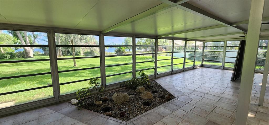 A screened-in porch features tile flooring, a central rock garden, and large windows overlooking a lawn — 7864 BROKEN ARROW TRAIL, WINTER PARK, FL