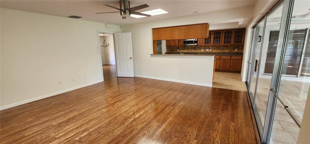 A living room with hardwood floors opens to a kitchen with wood cabinets and tile — 7864 BROKEN ARROW TRAIL, WINTER PARK, FL
