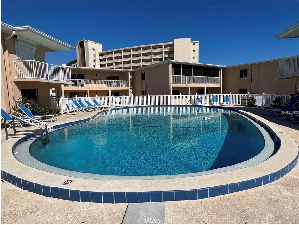 A swimming pool with blue tiles is surrounded by a concrete deck and apartment buildings — 573 N ATLANTIC AVENUE UNIT 5, NEW SMYRNA BEACH, FL