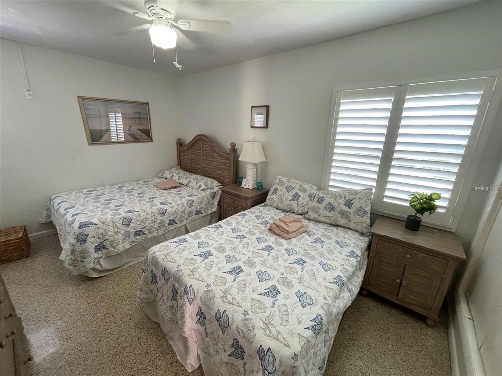 A bedroom features two beds with seashell-patterned bedding, a nightstand, and white window shutters — 573 N ATLANTIC AVENUE UNIT 5, NEW SMYRNA BEACH, FL