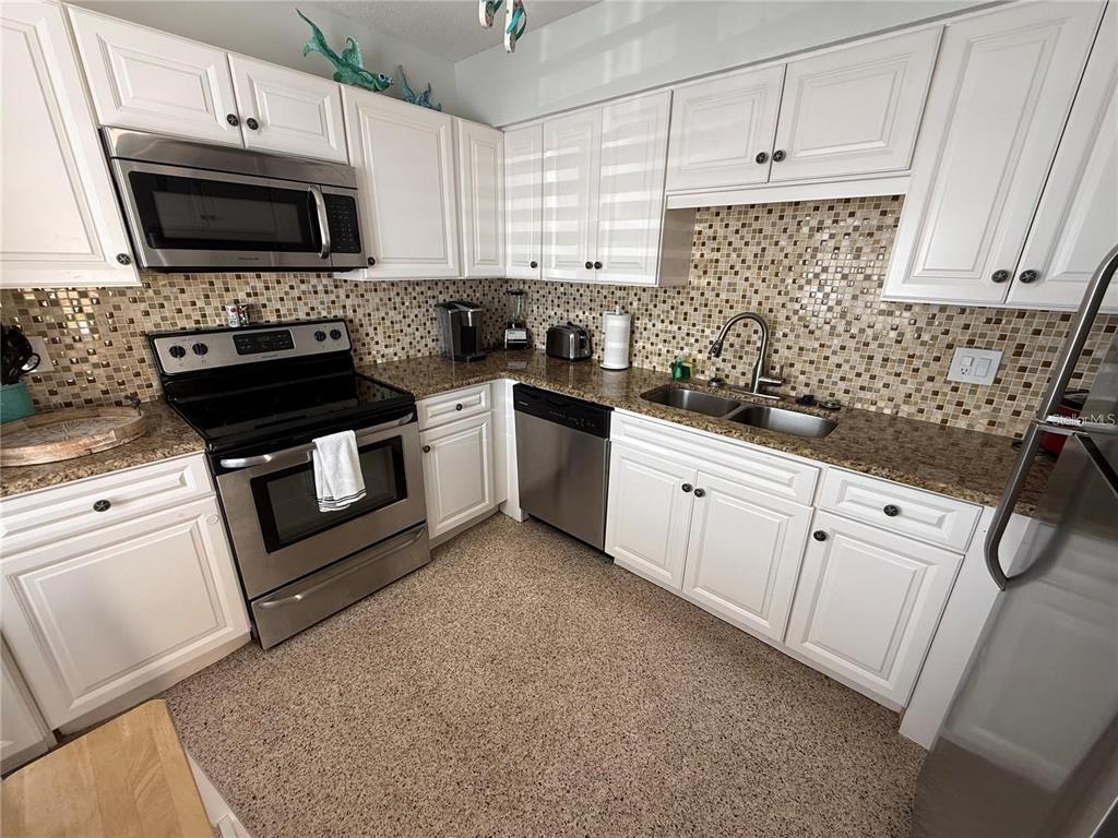 A kitchen features white cabinets, stainless steel appliances, granite countertops, and a mosaic tile backsplash — 573 N ATLANTIC AVENUE UNIT 5, NEW SMYRNA BEACH, FL