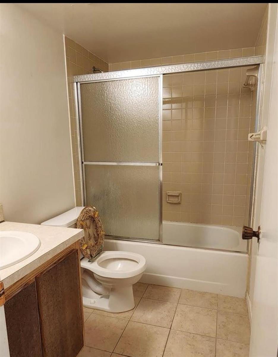 A bathroom features a tan tiled shower-tub combination, a white toilet, and a vanity cabinet — 1698 NE Sunny Brook Lane # G206, Palm Bay FL 32905, PALM BAY, FL
