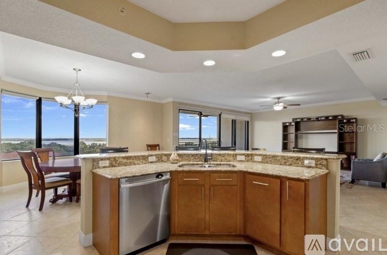 A kitchen island with granite countertops and a stainless steel dishwasher faces a dining area — 111 E MONUMENT AVENUE UNIT 705, KISSIMMEE, FL