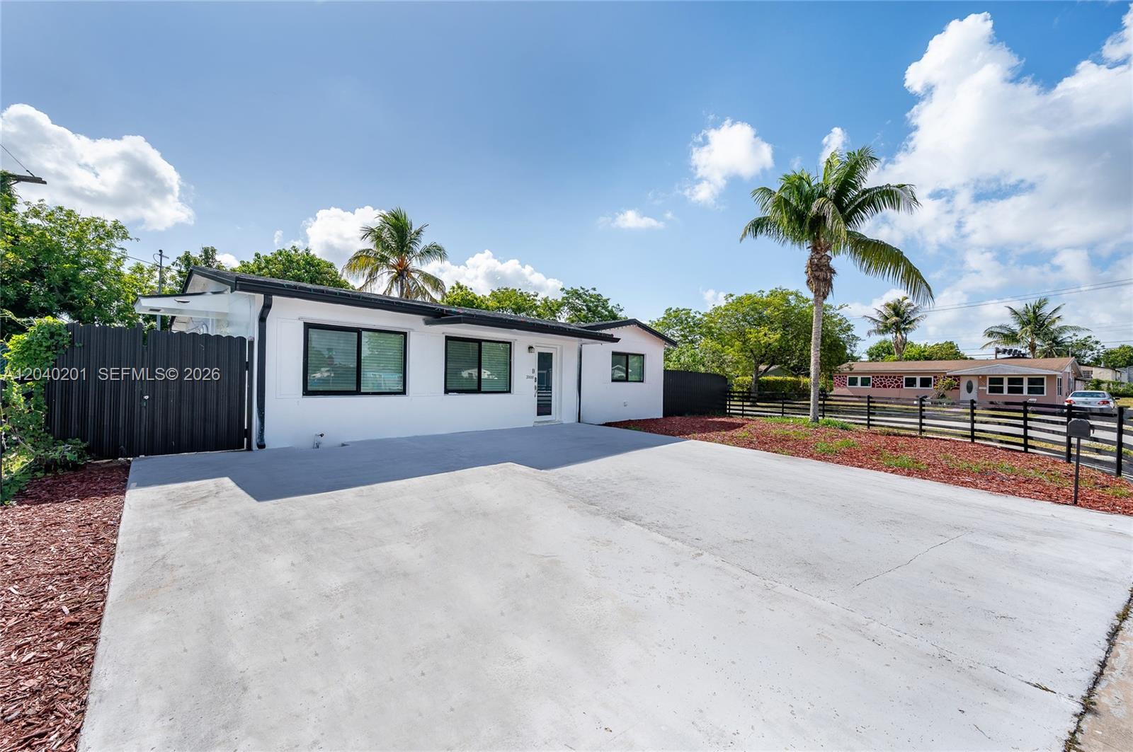 A white single-story house features a concrete driveway, black-framed windows, and a palm tree — 20001 NW 14th Ave, Miami Gardens FL 33169, MIAMI GARDENS, FL