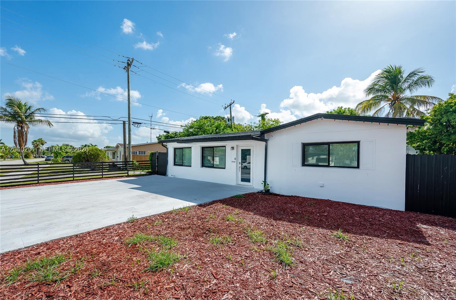 A white single-story house features a concrete driveway, black window frames, and red mulch landscaping — 20001 NW 14th Ave, Miami Gardens FL 33169, MIAMI GARDENS, FL