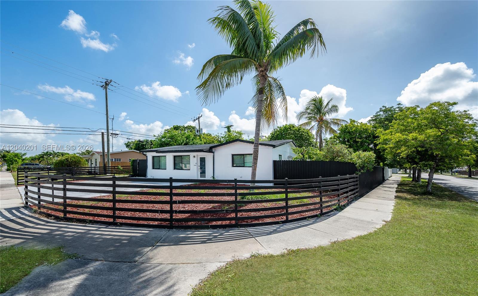 A white single-story house with a black fence and palm tree stands on a corner — 20001 NW 14th Ave, Miami Gardens FL 33169, MIAMI GARDENS, FL