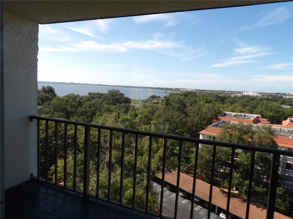 A balcony with a black metal railing overlooks a parking lot, trees, and a bay — 2699 SEVILLE BOULEVARD UNIT 802, CLEARWATER, FL