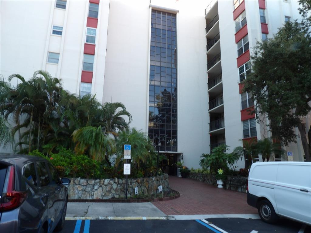 A multi-story apartment building exterior features a central glass-paneled stairwell and a brick-paved entrance — 2699 SEVILLE BOULEVARD UNIT 802, CLEARWATER, FL