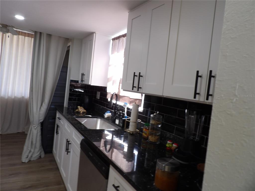 A kitchen features white cabinets, black countertops, and a black subway tile backsplash — 2699 SEVILLE BOULEVARD UNIT 802, CLEARWATER, FL