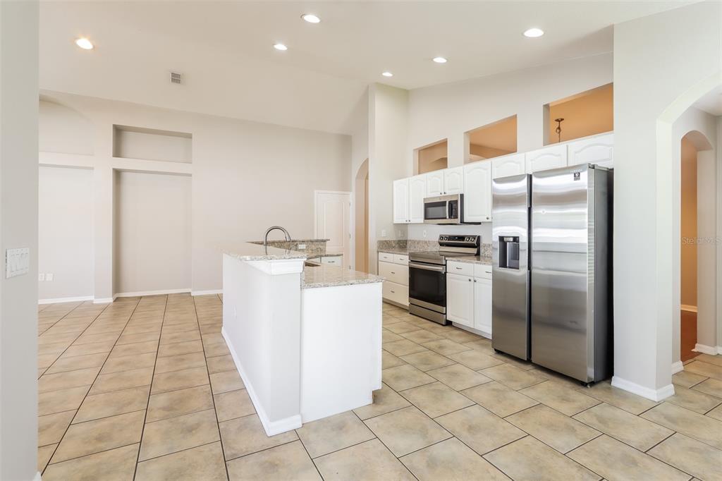 A kitchen with white cabinets, stainless steel appliances, granite countertops, and light-colored tile flooring — 23211 BAYOU GROVE STREET, LAND O LAKES, FL