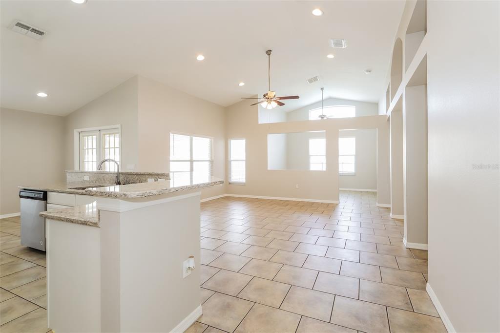 A kitchen with granite countertops overlooks a spacious living area with tile flooring and vaulted ceilings — 23211 BAYOU GROVE STREET, LAND O LAKES, FL