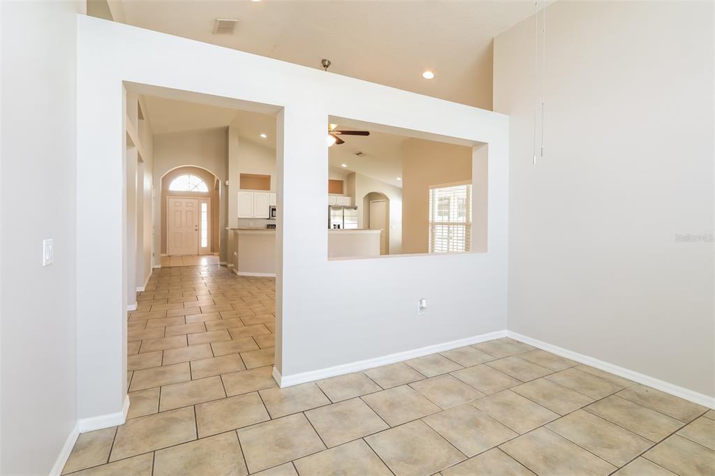 A tiled room features a large pass-through opening looking into a kitchen and entryway — 23211 BAYOU GROVE STREET, LAND O LAKES, FL