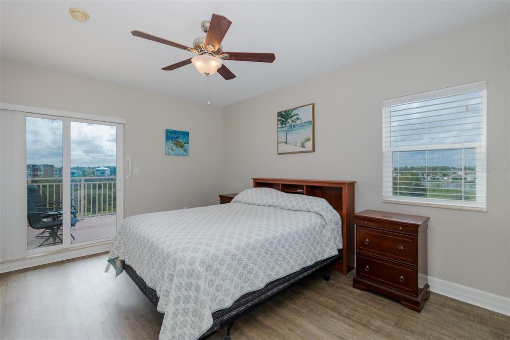 A bedroom features a bed with a wooden headboard, a ceiling fan, and a balcony — 4516 SEAGULL DRIVE UNIT 411, NEW PORT RICHEY, FL