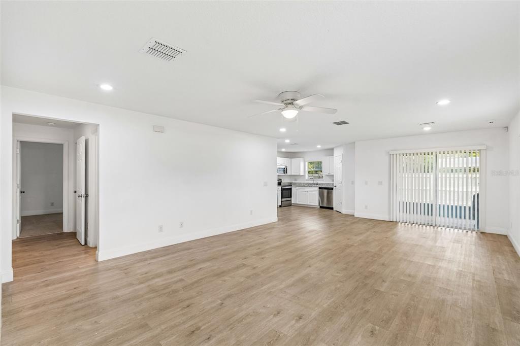 An open-concept living area features light wood-look flooring, white walls, and a kitchen in back — 5101 LANETTE STREET, ORLANDO, FL