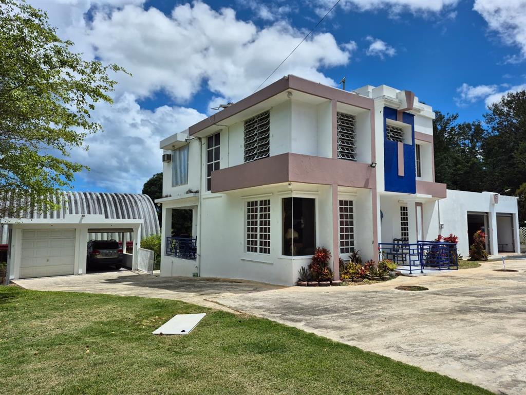 A two-story white house with blue accents, a concrete driveway, and a detached garage structure — Carr. 414, Km. 3.5 BO. CRUCES, RINCON, PR