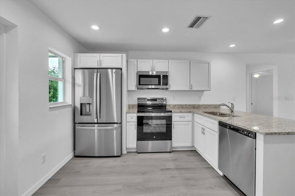 A kitchen features white cabinets, stainless steel appliances, and granite countertops over light wood flooring — 13101 SAN BENITO DRIVE, PUNTA GORDA, FL