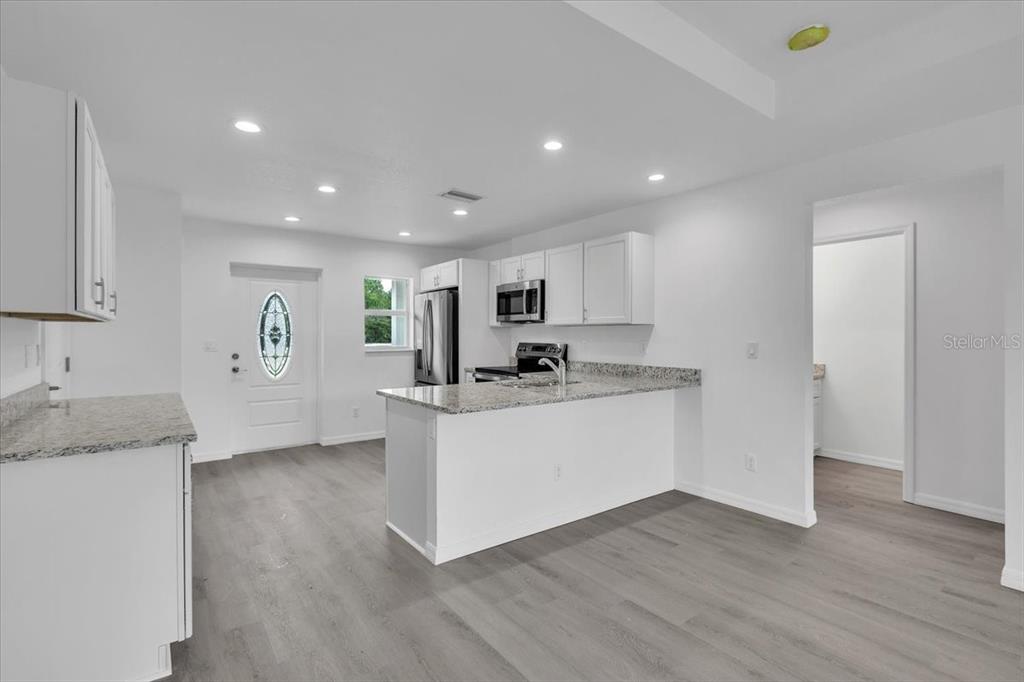 A kitchen with white cabinets, granite countertops, and light wood-look flooring — 13101 SAN BENITO DRIVE, PUNTA GORDA, FL