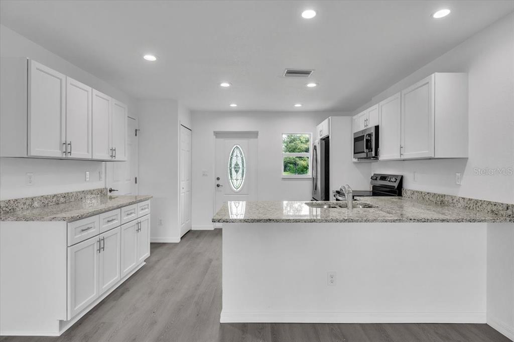 A modern kitchen features white cabinets, granite countertops, and light gray wood-look flooring — 13101 SAN BENITO DRIVE, PUNTA GORDA, FL