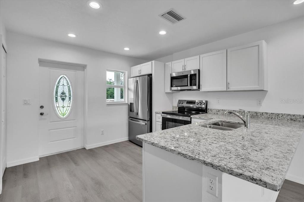 A modern kitchen features white cabinets, granite countertops, stainless steel appliances, and light wood flooring — 13101 SAN BENITO DRIVE, PUNTA GORDA, FL