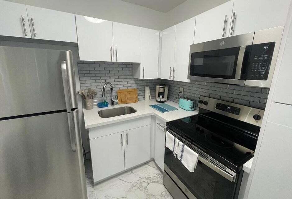 A compact kitchen features white cabinets, stainless steel appliances, a gray subway tile backsplash, and marble-patterned flooring — 201 S Ocean Boulevard # 7, Boca Raton FL 33432, BOCA RATON, FL