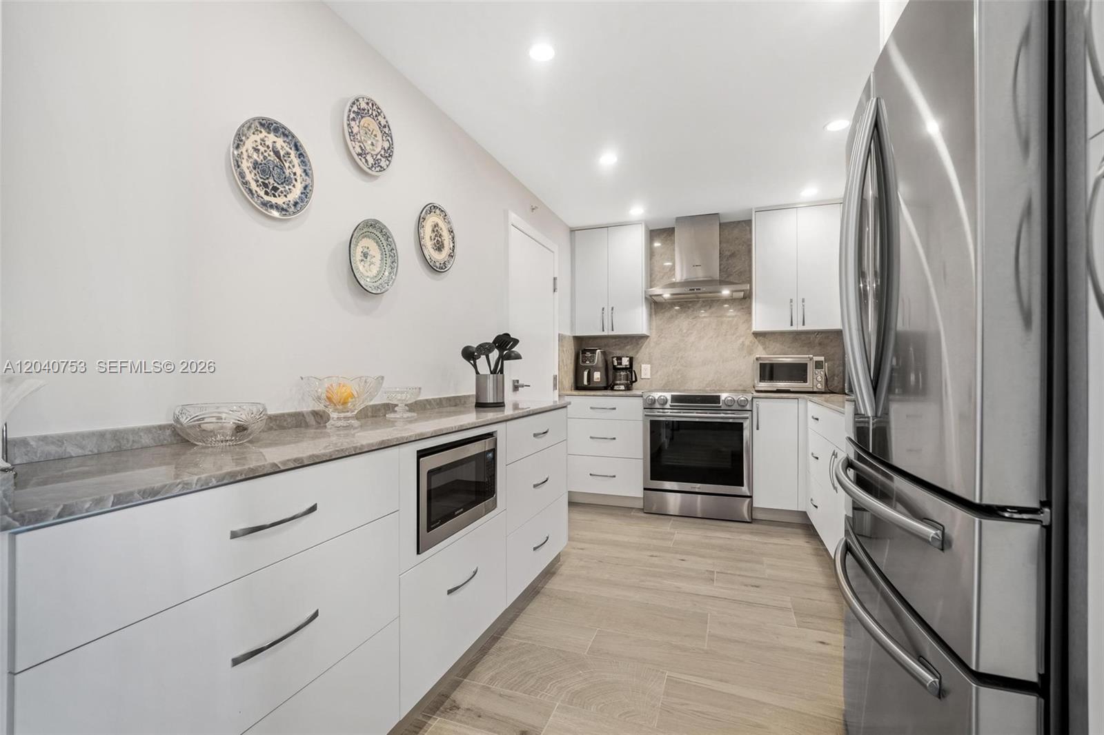 A modern kitchen features white cabinets, stainless steel appliances, and a gray stone countertop — 90 Edgewater Dr, Coral Gables FL 33133, CORAL GABLES, FL