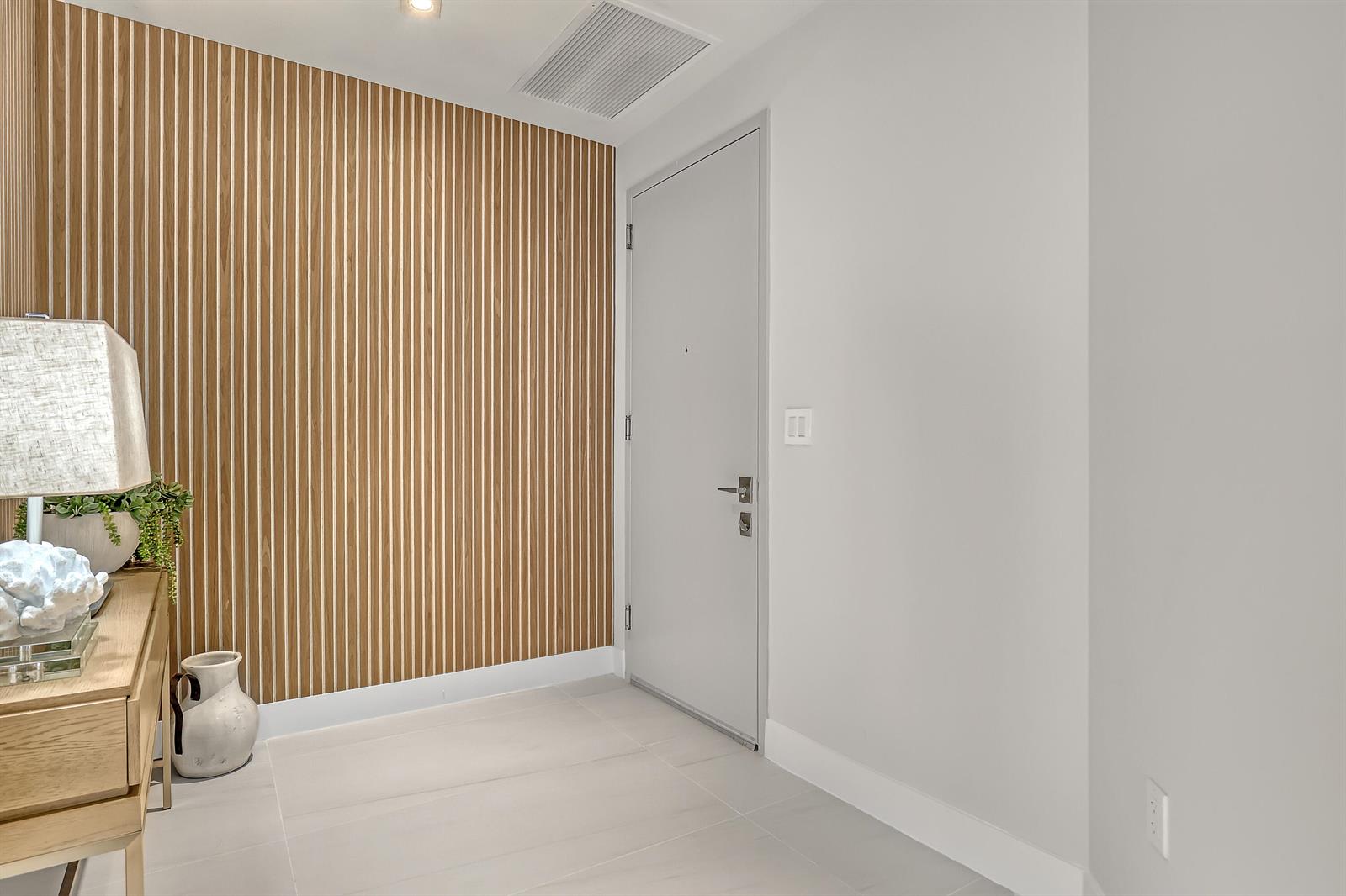 An entryway features a wood-slat accent wall, a light gray door, and a wooden console table — 3100 N Ocean Drive # 1703, Riviera Beach FL 33404, RIVIERA BEACH, FL