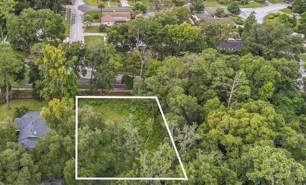 An aerial view shows a vacant, wooded residential lot outlined in white — 3112 NW 21ST STREET, GAINESVILLE, FL