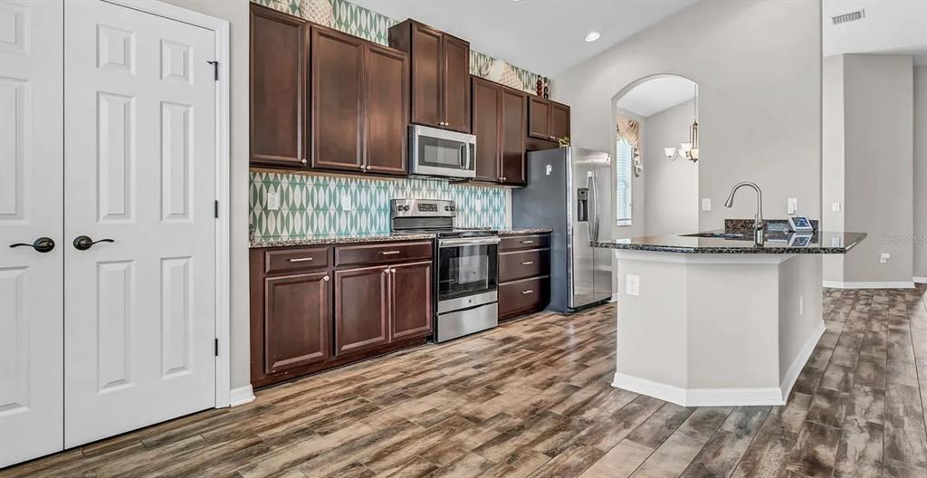A kitchen features dark wood cabinets, stainless steel appliances, a patterned backsplash, and an island — 7328 BLUE BEECH DRIVE, RIVERVIEW, FL