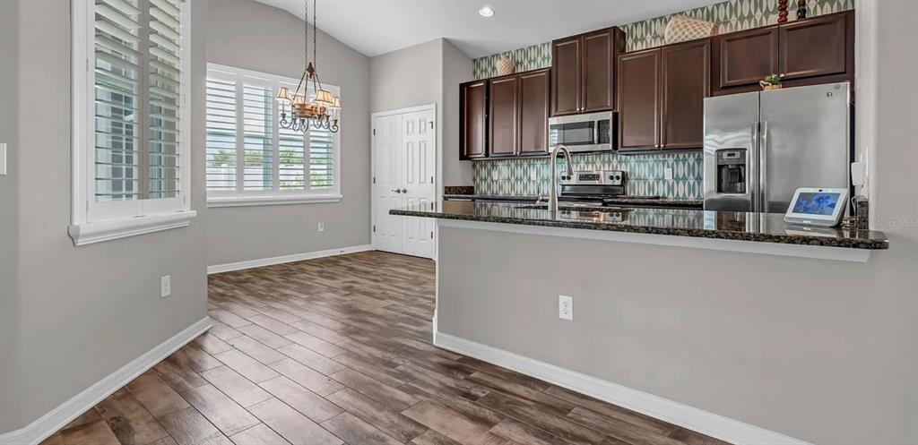 A kitchen with dark wood cabinets, granite countertops, and a dining area with plantation shutters — 7328 BLUE BEECH DRIVE, RIVERVIEW, FL
