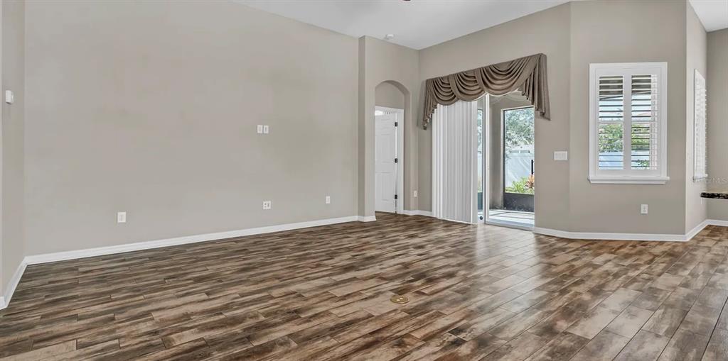 An empty living room features wood-look tile flooring, neutral walls, and a sliding glass door — 7328 BLUE BEECH DRIVE, RIVERVIEW, FL