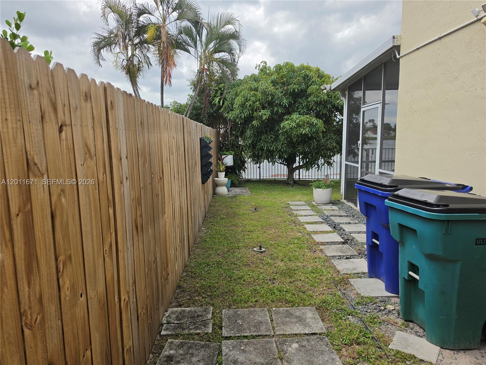 A side yard features a wooden fence, a grassy lawn, stone pavers, and two trash bins — 6178 Buena Vista Dr # 6178, Margate FL 33063, MARGATE, FL