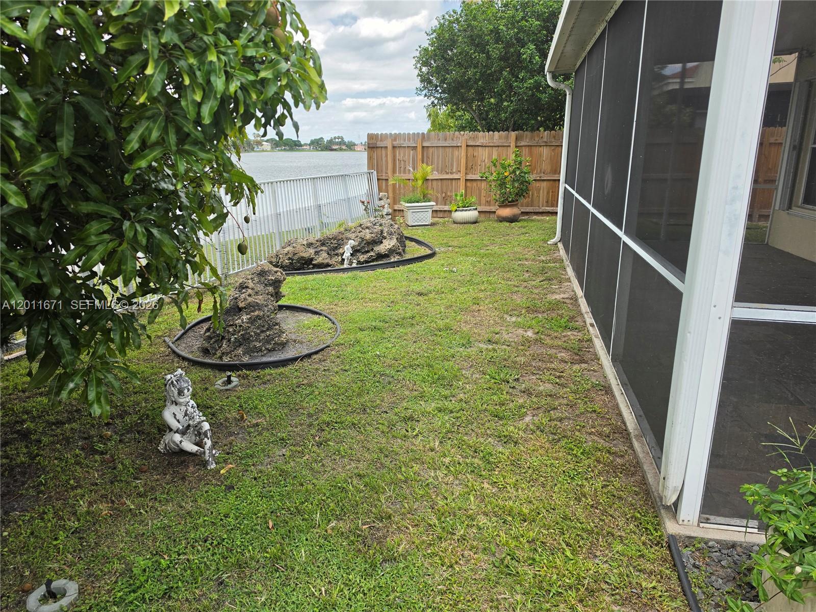A backyard features a grassy lawn, decorative rocks, potted plants, and a screened-in patio — 6178 Buena Vista Dr # 6178, Margate FL 33063, MARGATE, FL