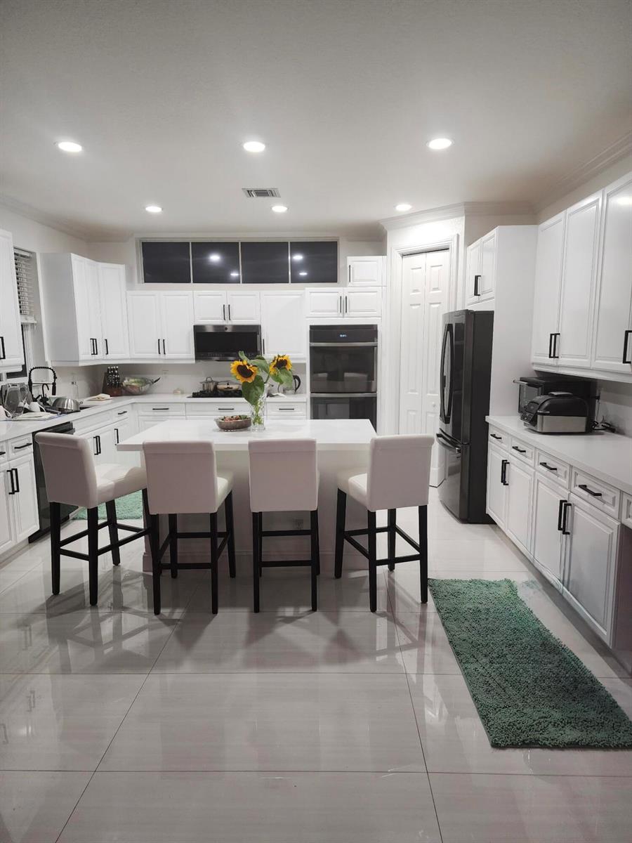 A white kitchen features a central island with four chairs, black appliances, and tile flooring — 400 SW 15th Drive, Boca Raton FL 33432, BOCA RATON, FL