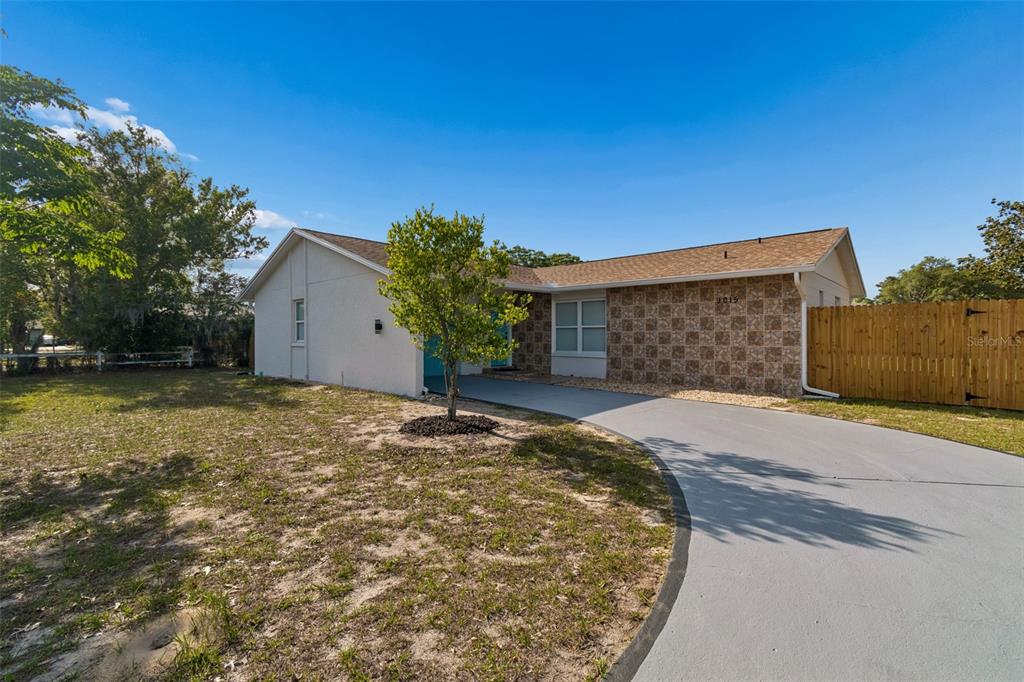 A single-story house with a light-colored exterior, stone facade, and a curved concrete driveway — 9015 FOREST OAKS BOULEVARD, SPRING HILL, FL