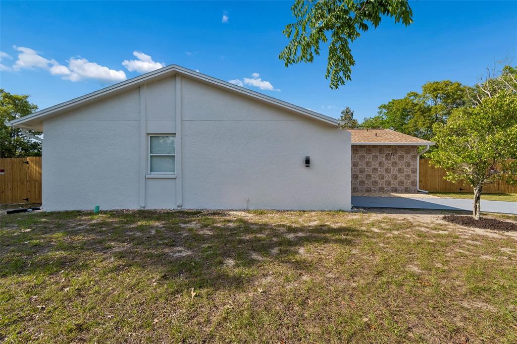 The exterior of a white stucco house features a single window and a stone-accented wall — 9015 FOREST OAKS BOULEVARD, SPRING HILL, FL
